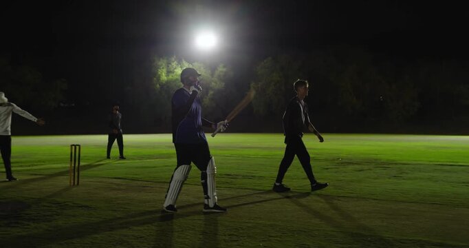 After reaching milestone, male teammates raising bats and exchanging high-fives, floodlight