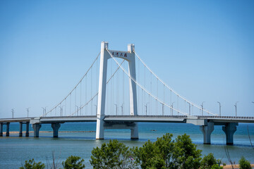Obraz premium White Suspension Bridge Spanning Coastal Water Under Clear Sky