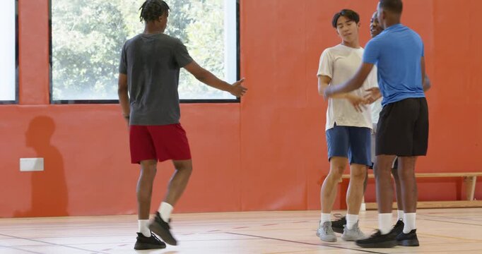 Dribbling basketball causing defender fall diverse male teammates, lifting up and resetting play