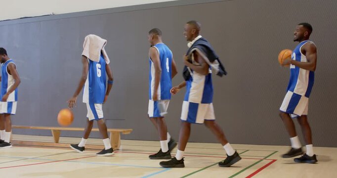 Carrying duffel into gym, five players sitting on bench chatting post practice