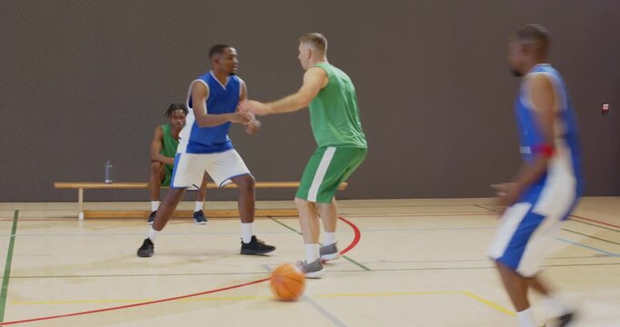 Diverse blue team players dribbling at green defenders, passing basketball to reset play in gym