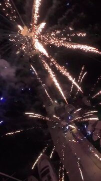 Vertical FPV drone flight through exploding fireworks at night, cinematic aerial view over harbor with boats, dynamic action footage 9x16.