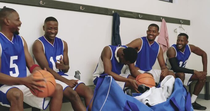 Welcoming newcomer, male basketball partners passing ball joking on locker room bench