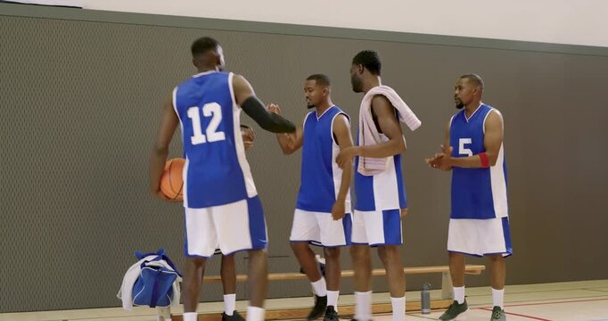 African american male players in uniforms standing up after captain spinning ball, clapping in gym