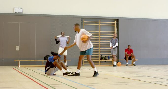 Male teammates dribbling basketball at gym using crossover helping defender, shooting jump shot