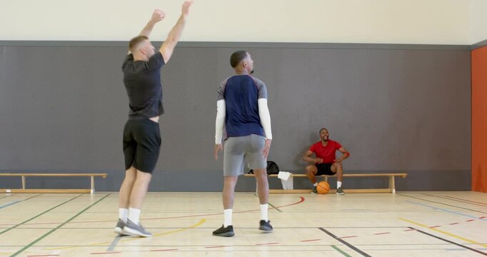 Diverse friends at gym dribbling ball, defender mirroring, faking shot, scoring, and shaking hands