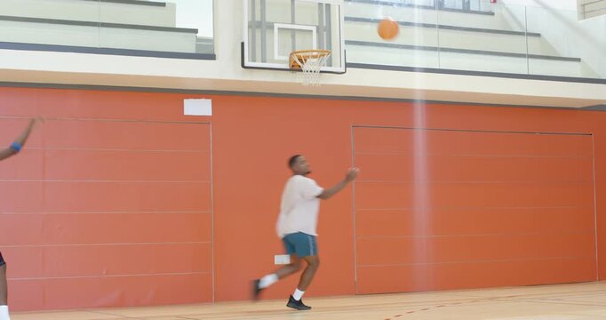African american male friends training at gym, crossover dribbling faking layup, and rebounding