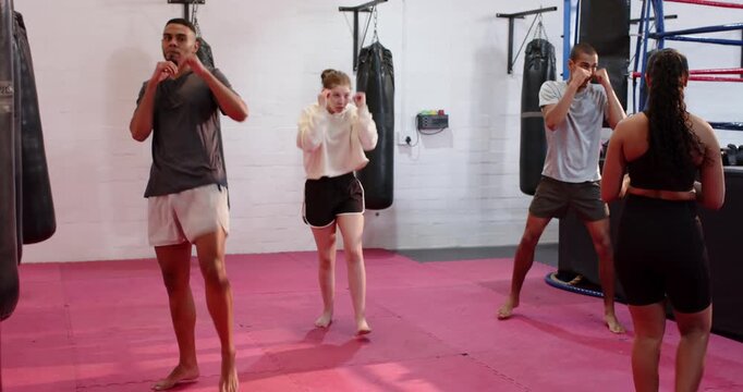 Diverse trainees mirroring warm-up punches and kicks after instructor cue on mat with punching bags
