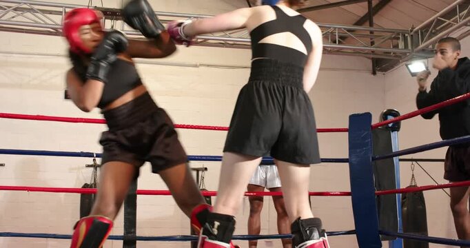 Bell spurring Two female boxers sparring in boxing ring, trading feints, jabs under coach guidance