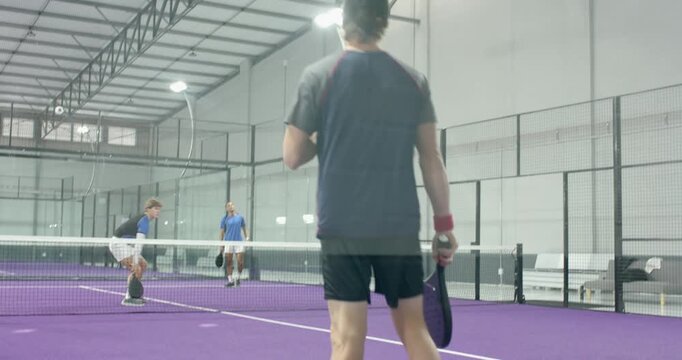 Man in shirt receiving opponents' shot, volleying padel ball on padel court to continue rally