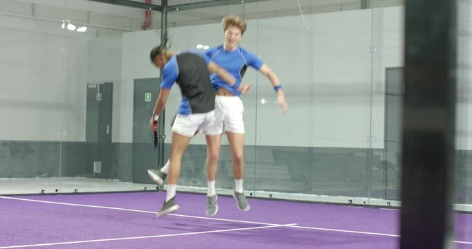 Lobbed ball causing diverse male duo volleying, picking ball and serving on padel court