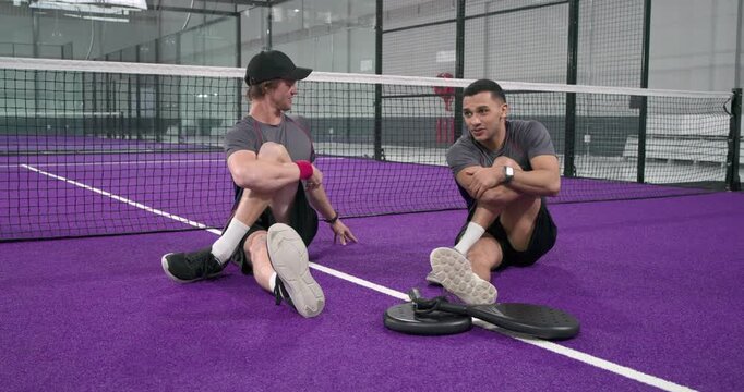 Diverse male friends switching knee-hug twist and forward-fold stretching on padel court