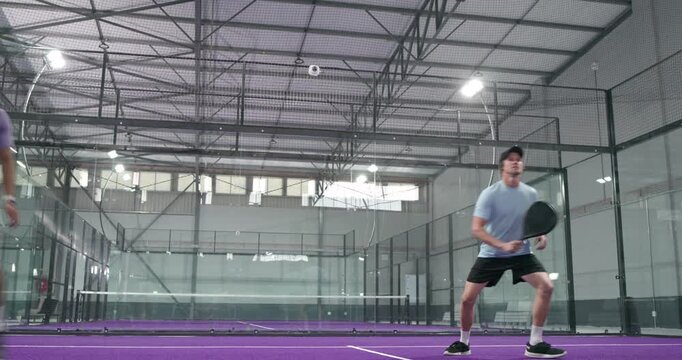 Male training partners tracking overhead lob with paddles and volleying forehand on court