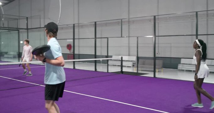 Diverse doubles teams returning serve and volleying padel ball to win point, tapping paddles