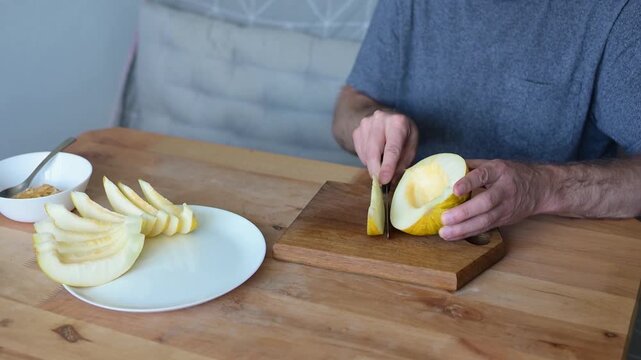 Man cutting yellow melon half with knife on wooden board in Full HD kitchen video