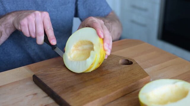 Man cutting yellow melon half with knife on wooden board in kitchen video Full HD