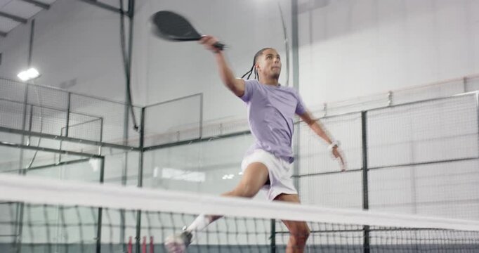 Man scanning incoming padel ball on glass court holding racket, smashing overhead to return shot