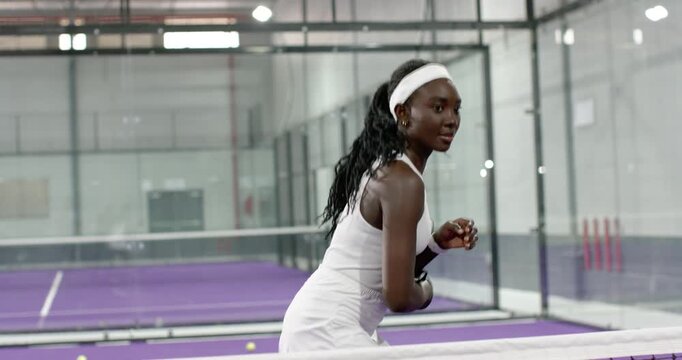 Mid adult woman with black racket tracking ball, returning forehand on purple padel court