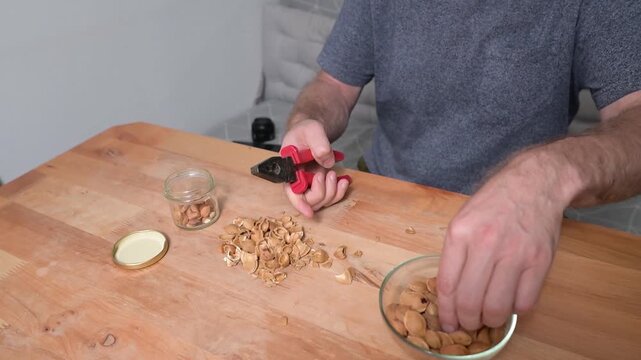 Man cracking apricot kernels with pliers at wooden kitchen table preparing healthy video Full HD ingredients