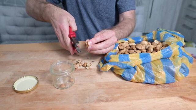 Man cracking almond shell with pliers at wooden table in home video Full HD kitchen