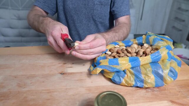Man cracking almond shell with pliers at wooden table in home kitchen video Full HD