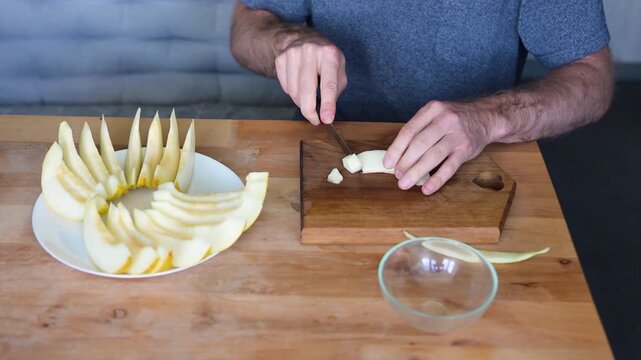 Man carving melon wedge and arranging fruit slices on white plate in video Full HD kitchen