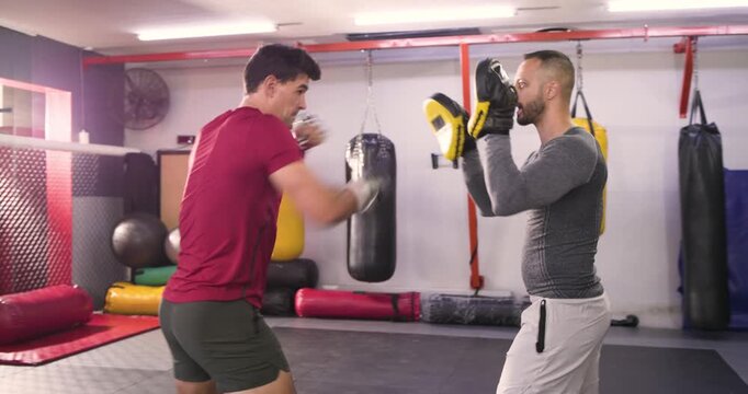 Indian coach holding mitts guiding mid-adult man boxer into combo punches at boxing gym