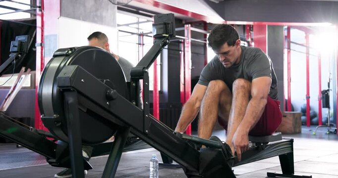 Diverse male friends entering crossfit gym, adjusting seats and securing feet on rowing machines