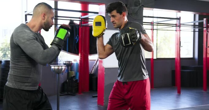 Boxing trainer and trainee signalling mitt drill at boxing gym testing reflexes and punching