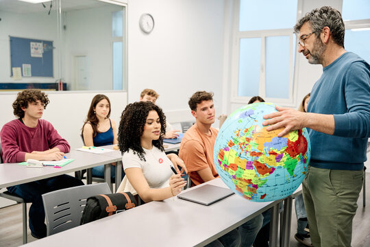 Geography teacher explaining world globe to university students