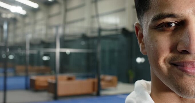 Teenage male in hoodie pivoting head, smiling at camera at gym with pit, copy space