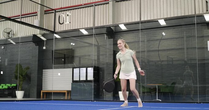 Female padel friends on court holding paddle tossing ball swinging serve cheering prepping