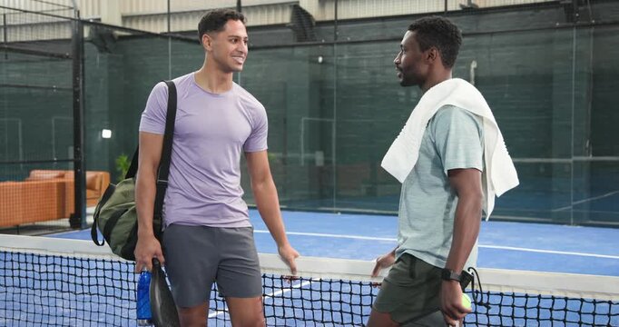 Diverse male friends meeting at padel net exchanging ball, recapping points after match ending