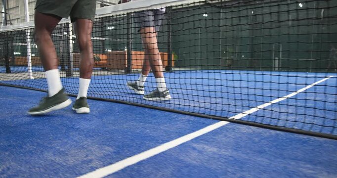 Diverse male padel players walking on court toward lounge couchs grabbing paddle preparing next set