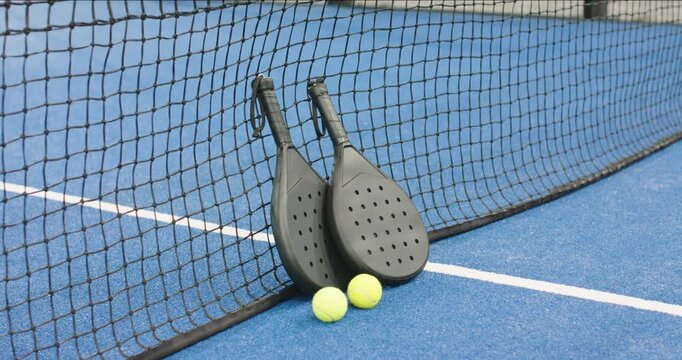 At clip start camera capturing padel rackets leaning against net with balls resting on court