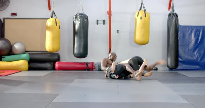 Diverse male training partners feinting jab taking takedown and securing side control in gym drill