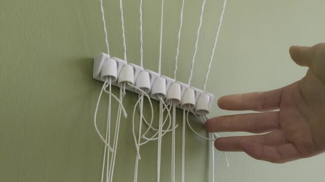 A hand waves near white strings hanging from a plastic holder mounted on a green wall. Concept of home organization hacks, DIY craft projects, and simple household inventions.