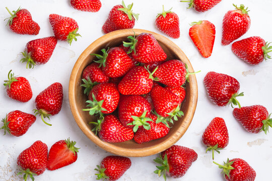 Bowl full of ripe strawberry top view with berries around on white rustic table surface background