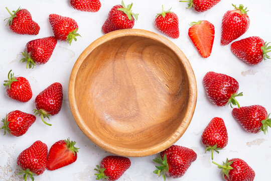 Empty bowl top view with whole and sliced ripe strawberry around on white rustic table textured background