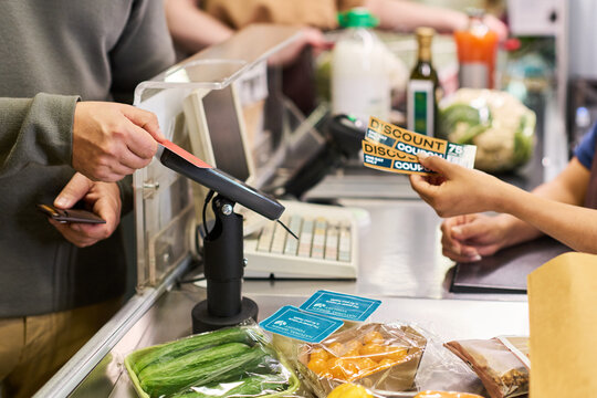 Cashier assisting customer checking out groceries and discount coupons at supermarket register, supporting retail service and consumer shopping marketing