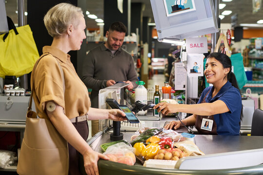 Adult woman with diabetes paying by smartphone at supermarket checkout, showing glucose sensor. Useful for healthcare retail, chronic condition management marketing