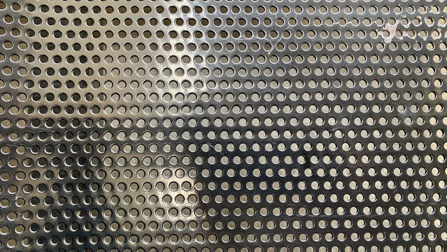 Close up of a grey perforated metal sheet texture. Abstract industrial background with a pattern of round holes.