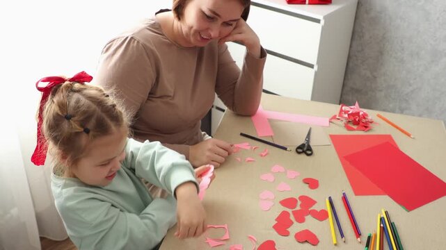 Young woman and small daughter creating crafts and inflating balloons together at home. Early childhood development, creativity, and family bonding concept.
