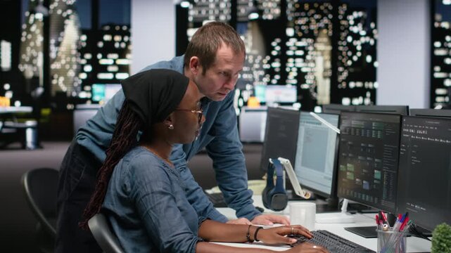 Manager supervising trainee typing code on computer, developing machine learning models to automate tasks in workspace. Team leader and intern writing programming language scripts on PC.