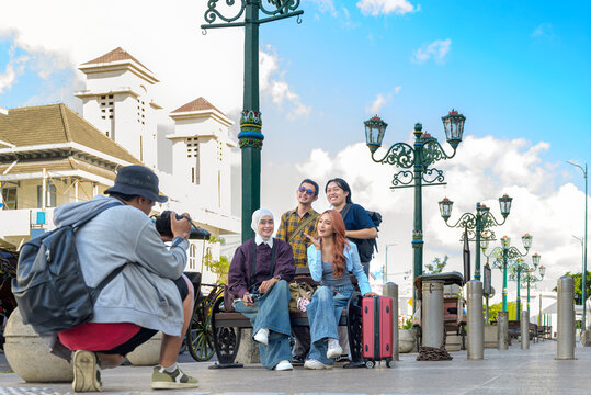 Indonesian southeast asian photographer taking a photo of young friends posing happily on a bench during their travel vacation in Yogyakarta, Indonesia. Travel or vacation concept