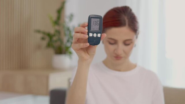A woman holds up a glucometer showing a blood sugar level of 136 mg dL. This reading indicates a high glucose level that may concern people with diabetes.