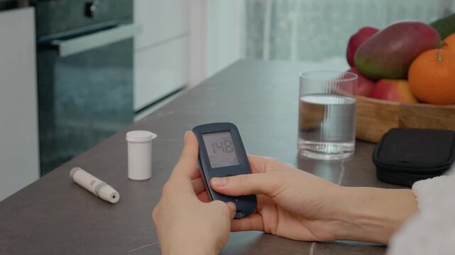 In a kitchen, a woman looks at the glucometer diary, swiping through past blood sugar results. She monitors her health by reviewing the glucose history carefully.