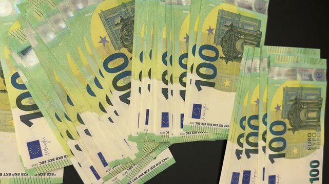 Counting large stack of 100 euro banknotes, cash falling onto black desk, close-up