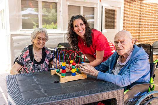 Caregiver assisting elderly residents with a brain stimulating bead maze game on a patio, promoting mental health and engagement