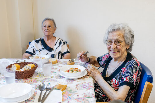 Senior women sitting at a table, smiling and sharing a meal, representing aging, care, and friendship in a retirement home